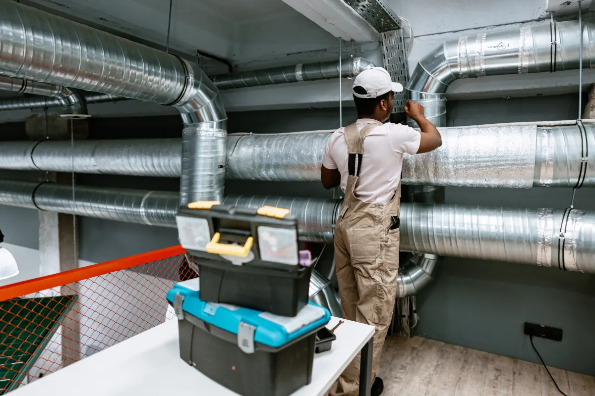 An Hvac Technician Is Installing Ductwork In A Modern Commercial Space During Daylight Hours